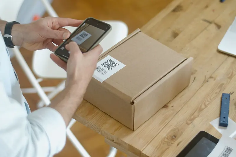 Ruce skenují telefonem QR kód na štítku papírové krabice